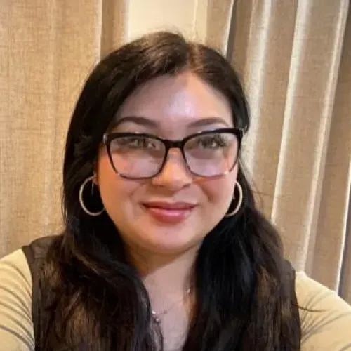 Latina woman in a yellow shirt poses in front of a curtain for a selfie