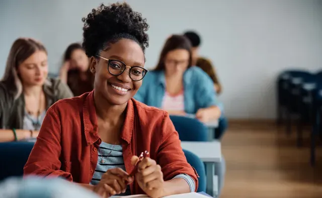 Happy African American woman attending a lecture in university classroom and looking at camera.